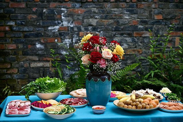 レンガの壁の前にblueのテーブルの上にバラが飾られていて、野菜・肉などの食材が置かれている